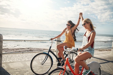 Two girls riding bikes by the beach