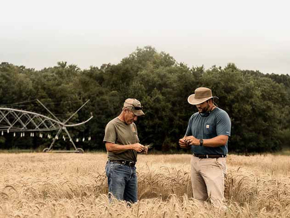 Two farmers standing in a field in front of an irrigation system